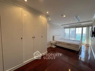 Spacious bedroom with large windows and wooden flooring, offering a serene view.