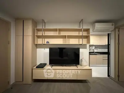 Modern living room with sleek wooden furniture and open kitchen layout, featuring a flat-screen TV and air conditioning.