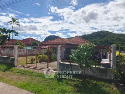 Charming suburban home with red-tiled roof and lush garden, nestled against scenic mountain backdrop.