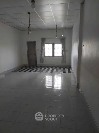Spacious empty room with tiled floor and large window, ideal for customization.