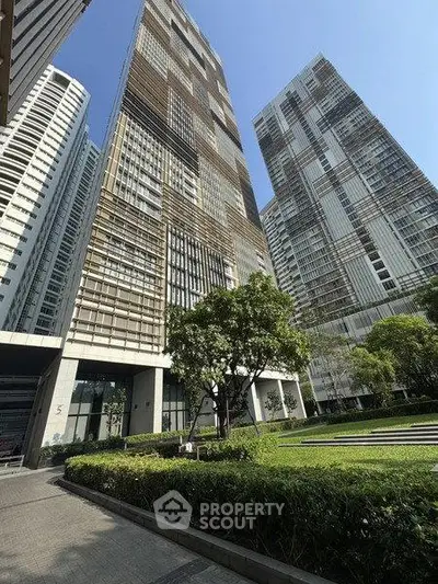 Stunning modern high-rise buildings with lush green landscaping and clear blue sky.