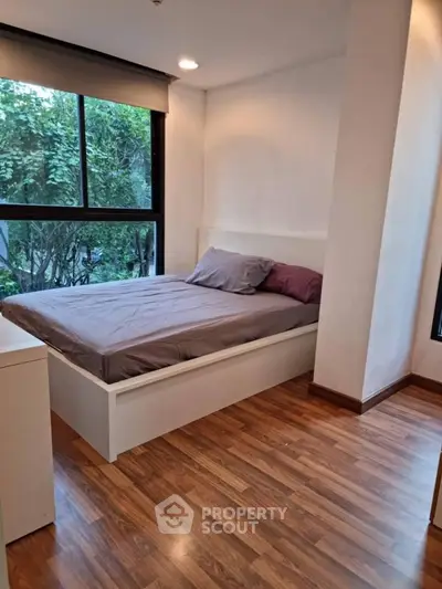 Cozy bedroom with large window and wooden flooring, perfect for relaxation.