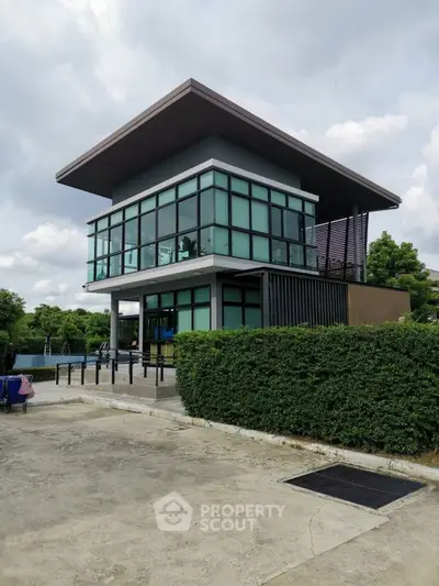Modern two-story building with large glass windows and lush greenery.