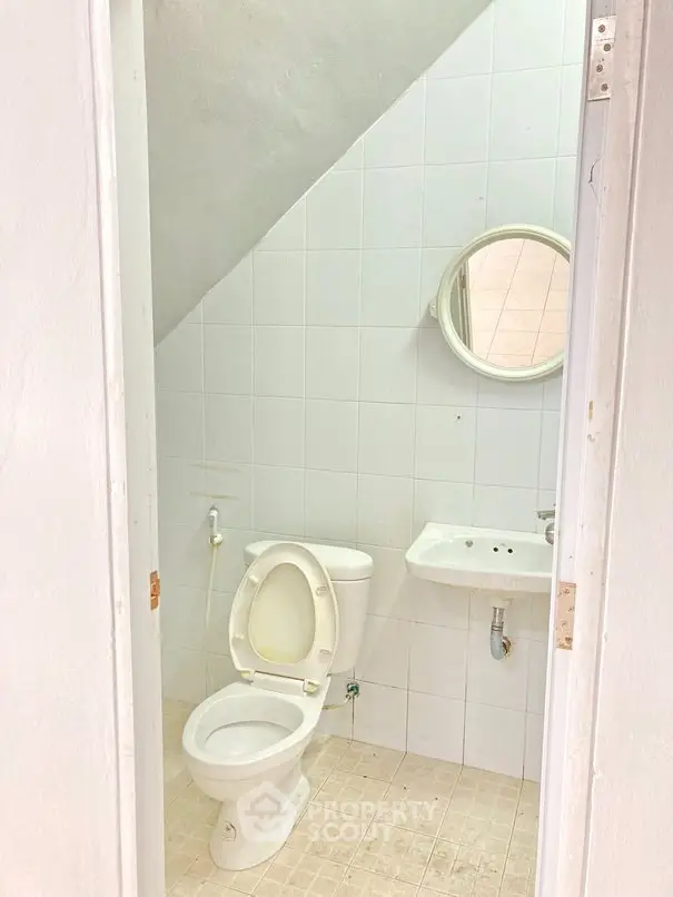 Compact bathroom with white tiles and basic fixtures under a sloped ceiling.