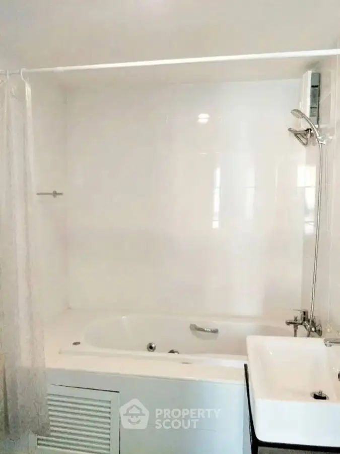 Modern bathroom with bathtub and shower, featuring sleek white tiles and a compact sink.
