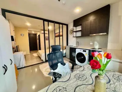 Modern studio apartment with sleek kitchen and cozy living area, featuring a washing machine and stylish decor.