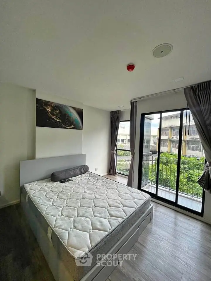 Spacious bedroom with large window and balcony access, featuring modern decor and ample natural light.