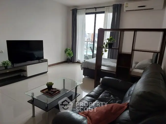 Spacious and well-lit living room with sleek leather sofa, modern entertainment unit, and glass coffee table, complemented by large windows.