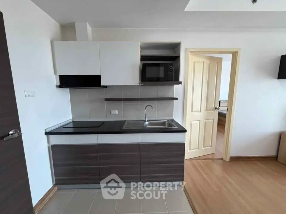 Modern compact kitchen with sleek cabinetry and built-in microwave in a cozy apartment.