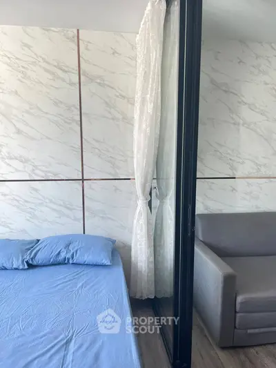 Modern bedroom with marble accent wall and cozy sofa, featuring elegant curtains and blue bedding.