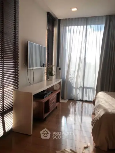 Modern bedroom with large window and sleek TV setup, featuring elegant wooden flooring.