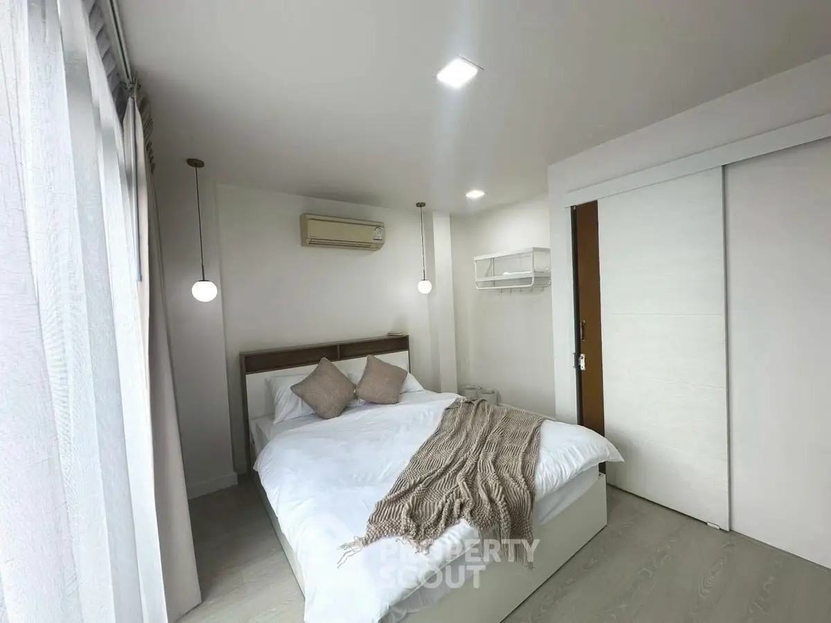 Modern bedroom with cozy decor and natural light, featuring a comfortable bed and stylish lighting.