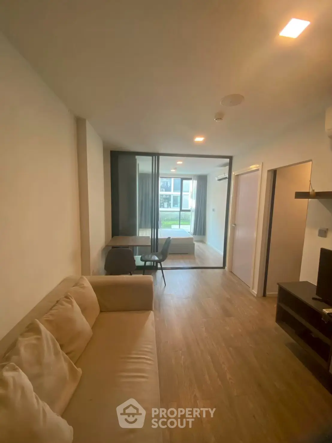 Modern living room with cozy sofa and glass partition leading to a bright bedroom.