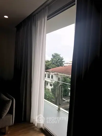 Spacious balcony view from modern apartment with elegant curtains and lush greenery.