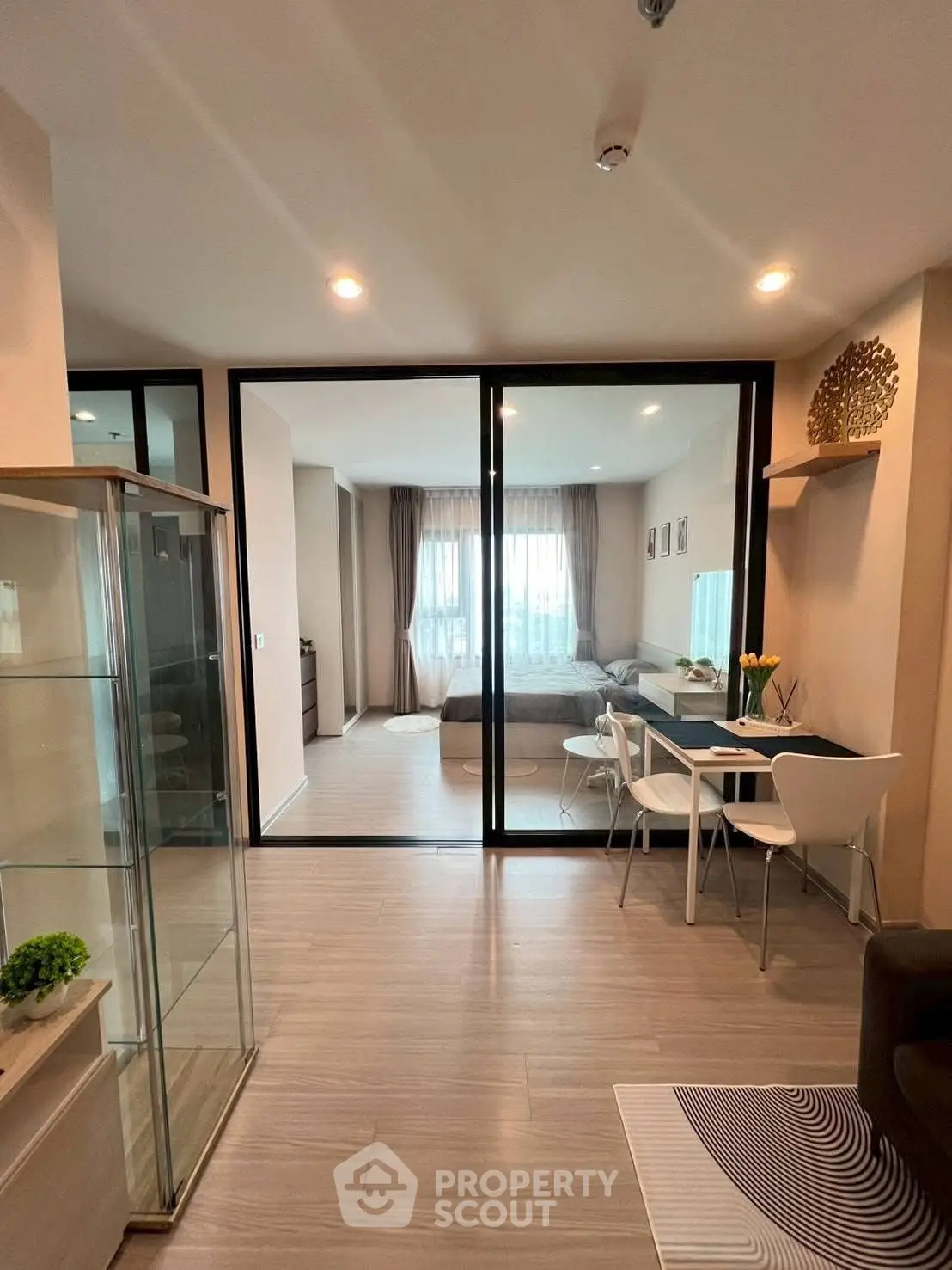 Modern open-plan living room with dining area and glass partition, featuring stylish decor.