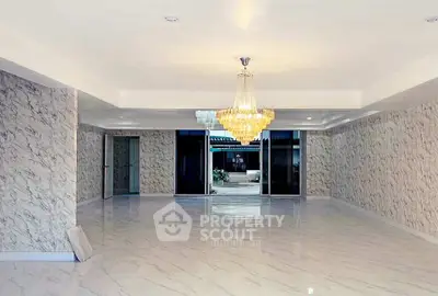 Spacious marble-floored room with elegant chandelier and large windows offering natural light.