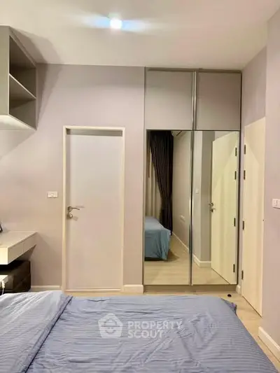 Modern bedroom with sleek design and mirrored closet doors, featuring a cozy bed and neutral tones.