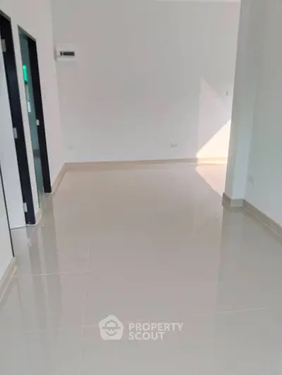 Spacious empty room with glossy tiled flooring and white walls, ideal for customization.