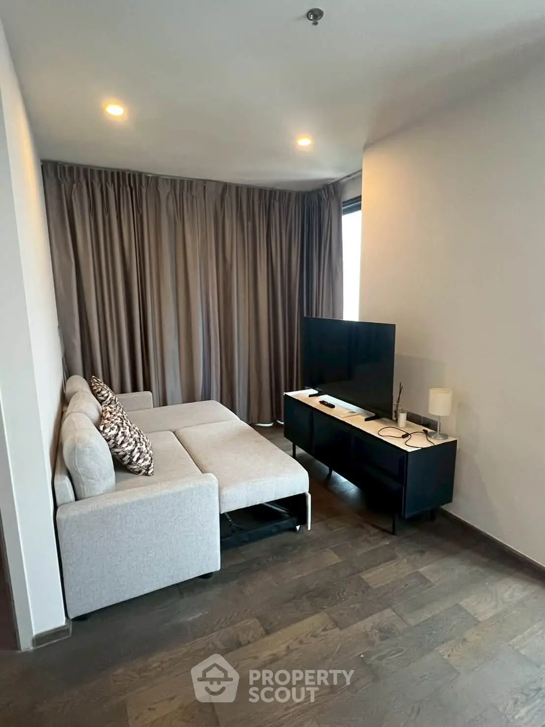 Modern living room with cozy sofa and flat-screen TV, featuring elegant curtains and wooden flooring.