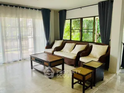 Spacious living room with elegant wicker furniture and large windows offering lush garden views.