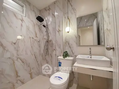 Modern bathroom with marble tiles, sleek fixtures, and a large mirror, showcasing elegant design and functionality.