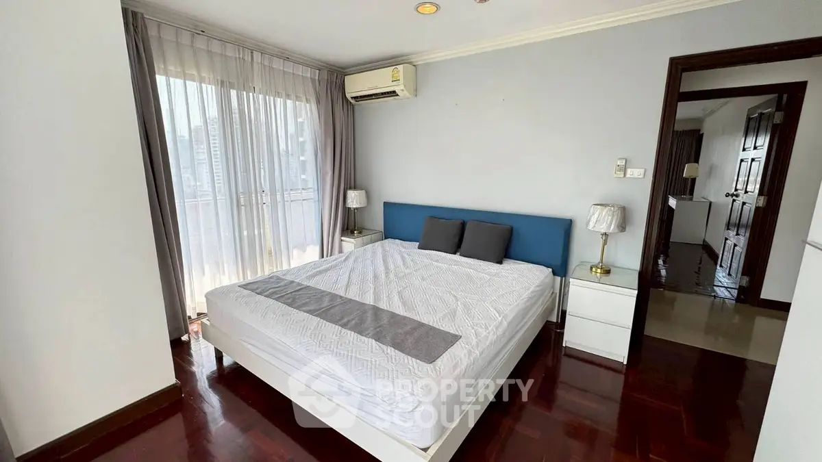 Spacious bedroom with city view and modern furnishings in a high-rise apartment.