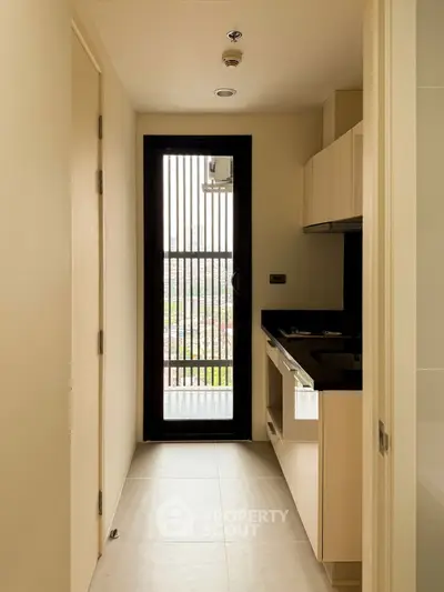Modern compact kitchen with sleek cabinetry and city view through vertical window slats.