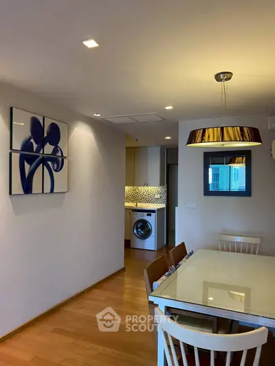 Modern dining area with stylish lighting and open view to kitchen with washing machine.