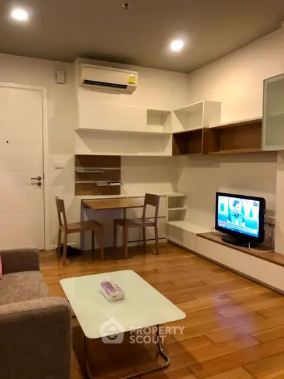 Modern living room with sleek furniture and wooden flooring, featuring a TV and air conditioning.