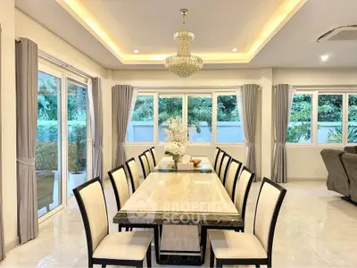 Elegant dining room with chandelier and large windows offering lush garden views.