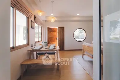 Charming open-plan living and dining area with natural wood accents and round window.