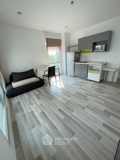 Modern studio apartment with sleek kitchen and cozy seating area, featuring stylish flooring and ample natural light.