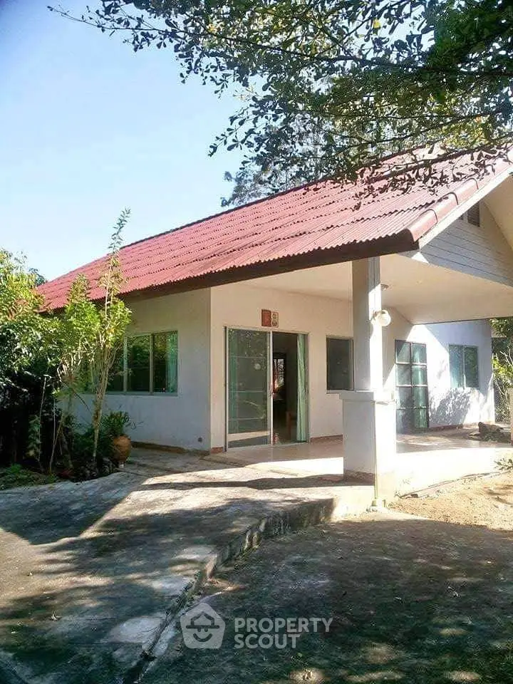 Charming single-story home with red roof and spacious front porch in a serene setting.