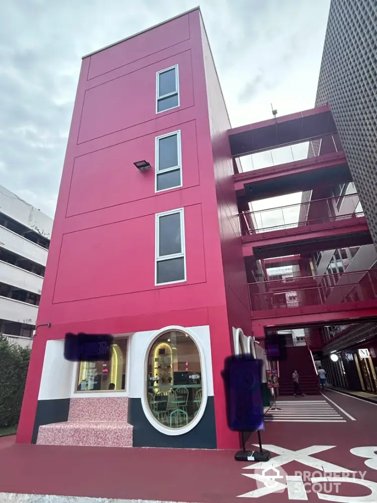 Vibrant pink modern building exterior with unique architectural design and circular window feature.