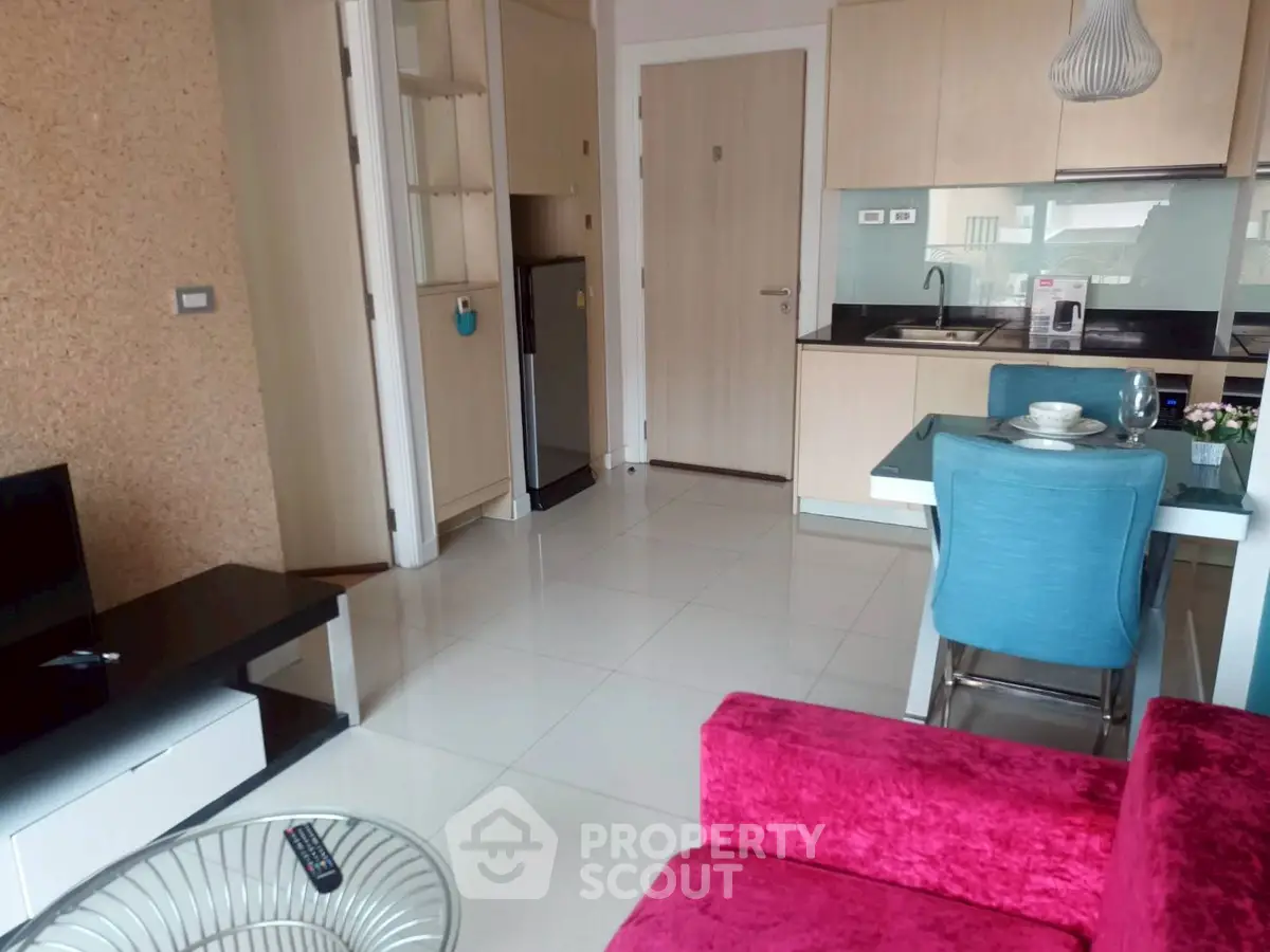 Modern open-plan living room with vibrant pink sofa and sleek kitchen area.