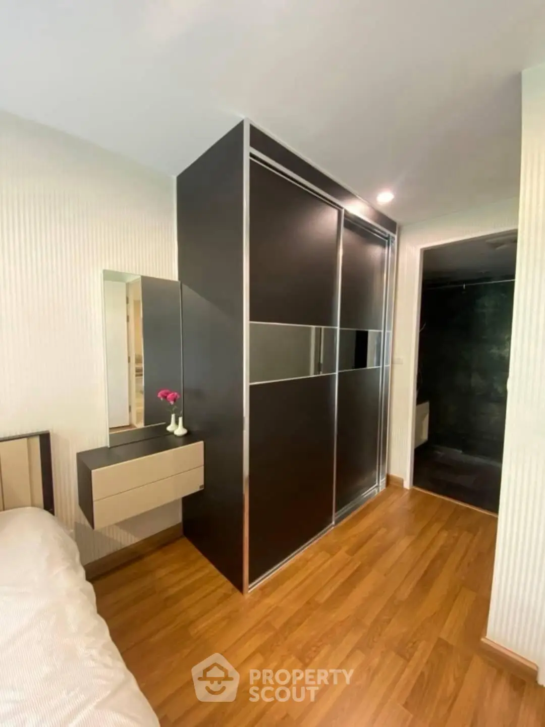 Modern bedroom with sleek wardrobe and wooden flooring, featuring a stylish vanity area.
