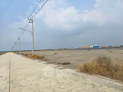 Expansive industrial land with paved road and utility poles, ideal for development opportunities.