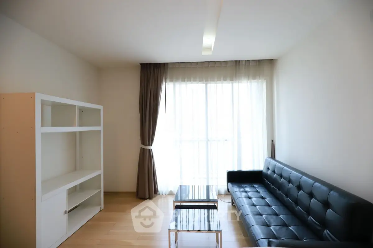 Modern minimalist living room with sleek black sofa and large window for natural light.
