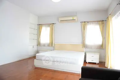 Spacious bedroom with hardwood floors and natural light, featuring a modern bed and air conditioning.