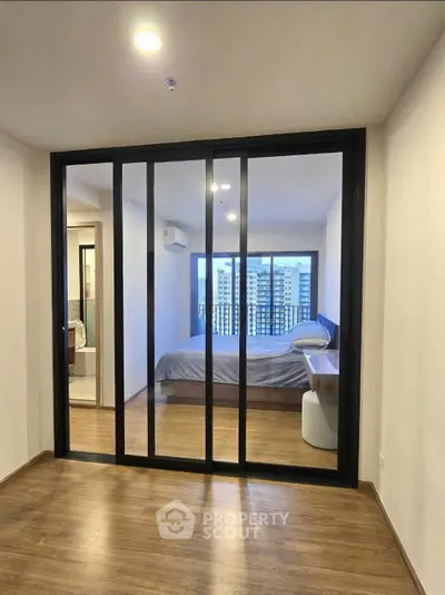 Modern bedroom with sliding glass doors and city view, featuring sleek design and natural light.