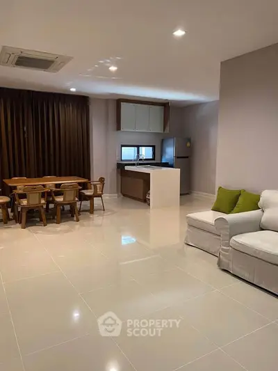 Spacious living room with modern open kitchen and dining area, featuring sleek tile flooring and cozy seating.