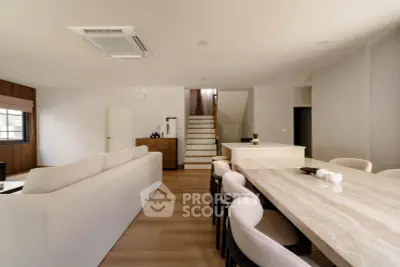 Spacious modern living room with elegant dining area and staircase, featuring neutral tones and sleek design.