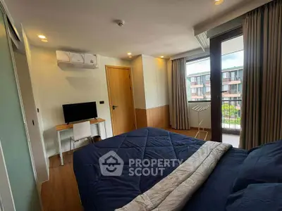 Modern bedroom with balcony view, featuring cozy bedding and a workspace, ideal for urban living.