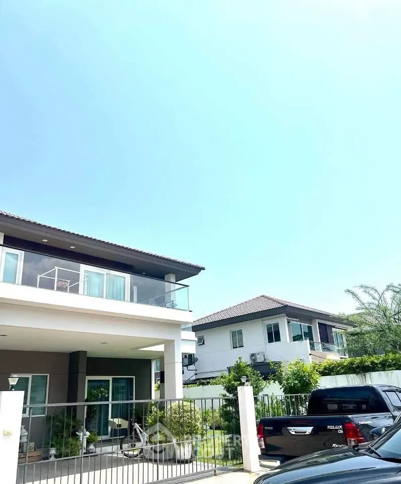 Modern two-story house with balcony and driveway in a sunny neighborhood.