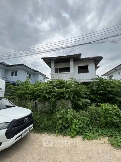 Unfinished two-story house with overgrown greenery in a suburban neighborhood, showcasing potential for renovation.