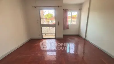 Spacious empty room with polished wooden floors and large windows offering natural light.