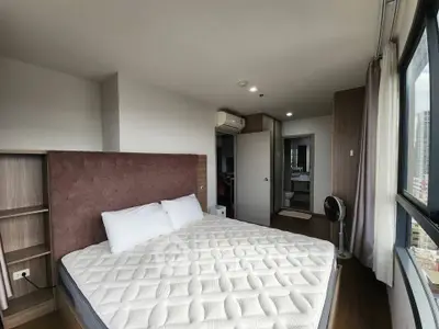 Spacious bedroom with large window and modern furnishings in a high-rise apartment.