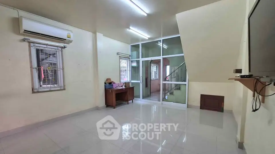 Spacious living room with air conditioning and modern lighting, featuring a sleek glass partition and staircase view.
