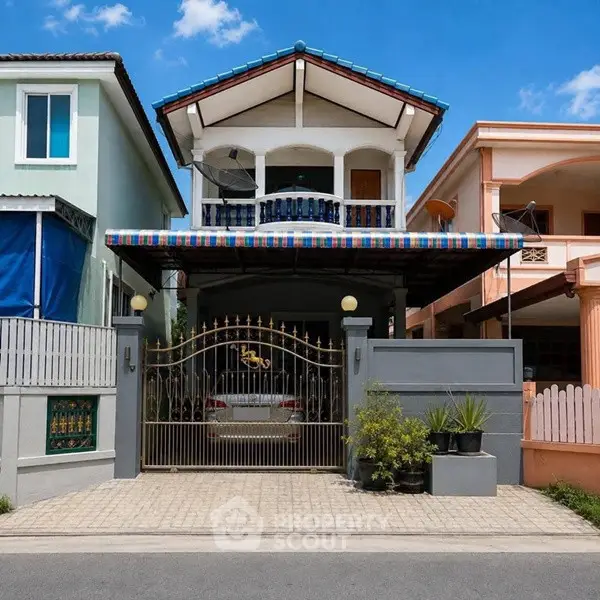 Charming two-story house with gated driveway and colorful awning in a suburban neighborhood.