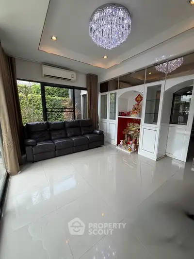 Elegant living room with modern chandelier and large windows offering lush garden views.